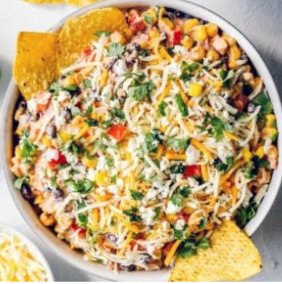 dip of sweetcorn and black beans with avocado and tomato in a base of mayonnaise and salsa served topped with grated cheese and coriander