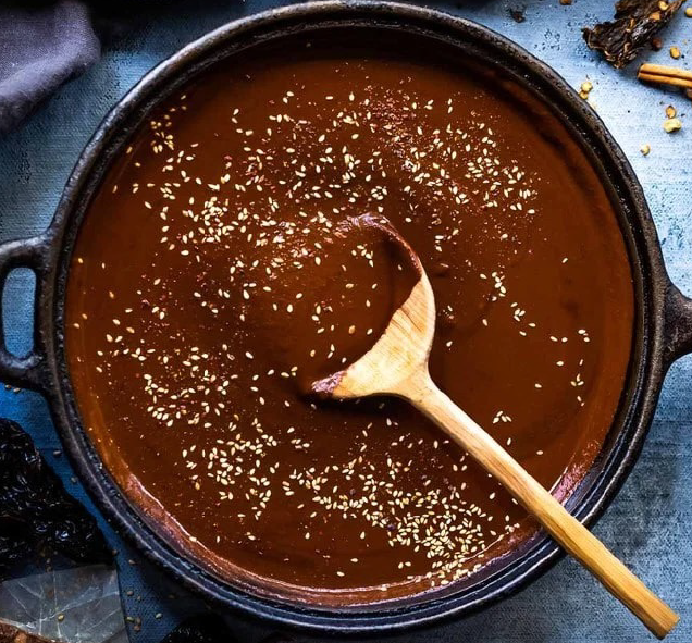 mole negro garnished with sesame seeds in a frying pan with a wooden spoon