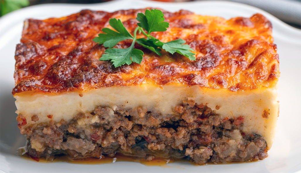 rectangle of Cypriot moussaka on a white plate with a flat-leaf parsley garnish