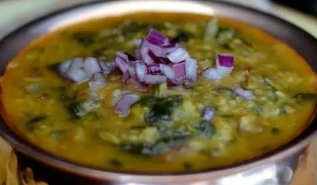 spinach and moong dal curry served in a copper dish and topped with chopped red onion