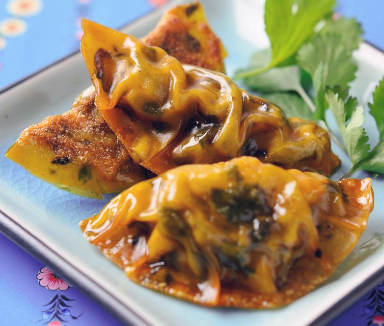 Three peking-style vegetable dumplings on a square white plate with a coriander garnish