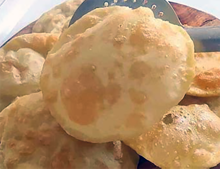 puffed puri or pooree flatbread lifted with a metal slotted spoon onto a pile on a wooden board