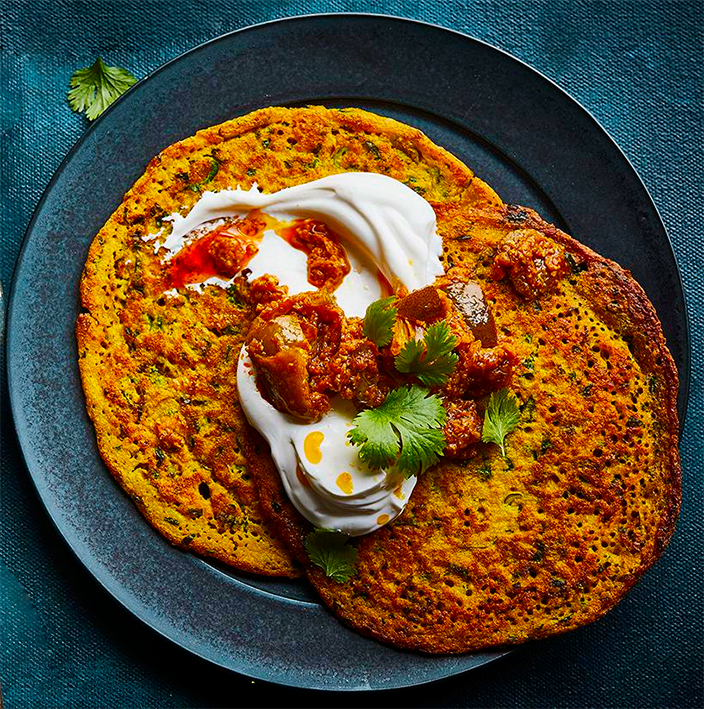 two red lentil pancakes served on a blue plate with a garnish of greek yoghurt and pickle
