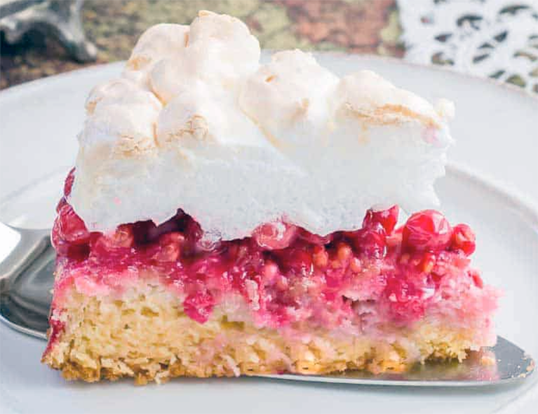 wedge of cake with a sponge base, redcurrant filling and meringue topping on a cake slice