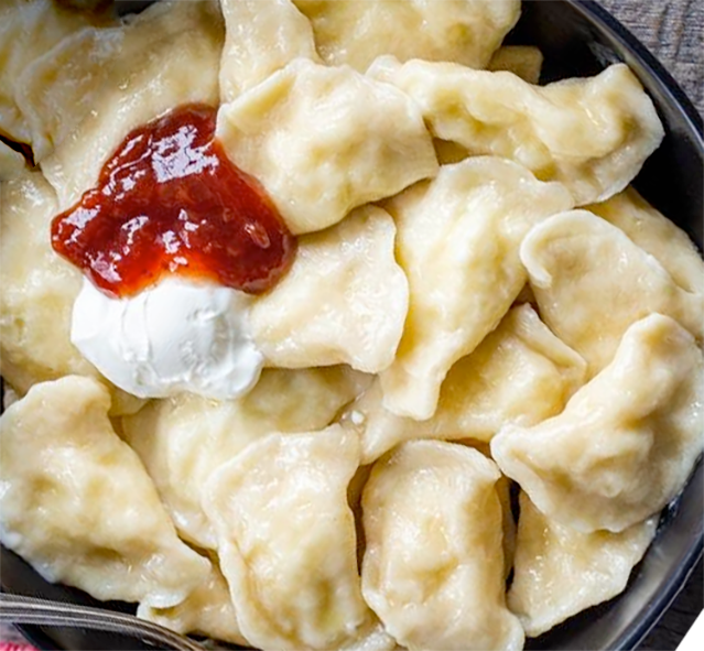 Russian pierogi in a bowl with a garnish of jam and soured cream