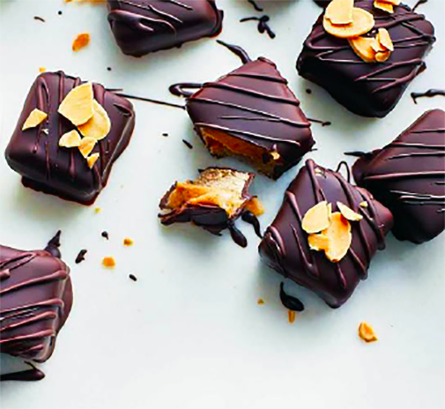 date, almond butter and coconut milk caramels on an oat base cut into squares and dipped in dark chocolate wth toasted almond topping