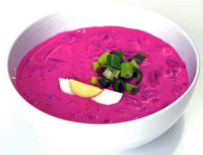 cold beetroot and kefir soup served in a bowl with a spring onion and onion wedge garnish