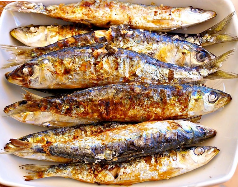 seven grilled sardines arranged on a white serving dish