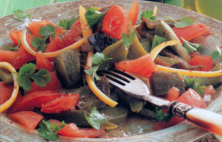 schalada, a salad of bell pepper, tomato, garlic and preserved lemon strips garnished with herbs and served on a plate with a fork