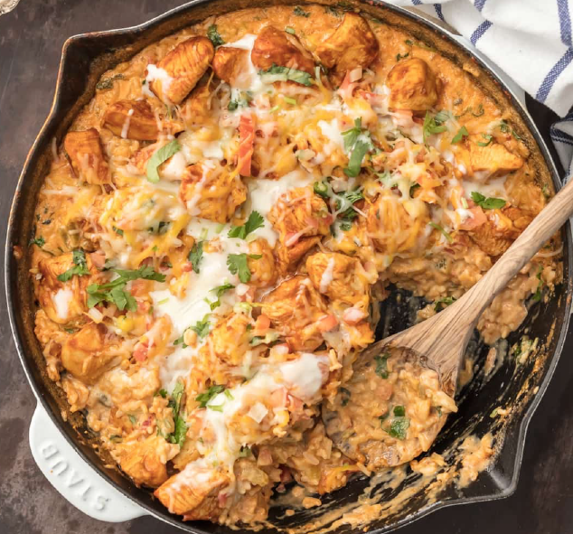chicken con queso, a dish of cheesy rice with coriander, pico de gallo, green chillies, topped with taco-spiced chicken in a steel pan