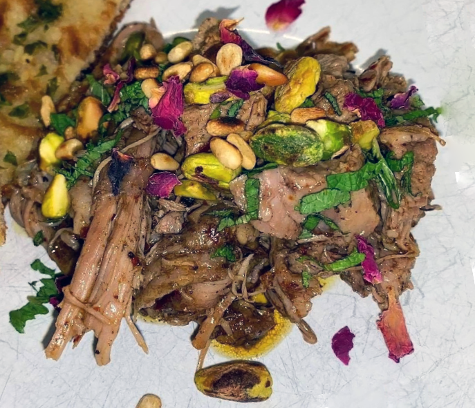 shredded slow-roasted lamb served garnished with herbs, nuts and pomegranate seeds