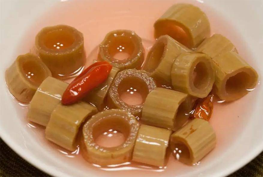 pipe-like pieces of japanese knotweed pickle in a bowl with a birds eye chilli as garnish
