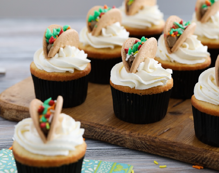 taco-topped cupcakes on a chopping board. Cupcakes with meringue buttercream icing and a decoration of a halved biscuit with filling resembling a taco