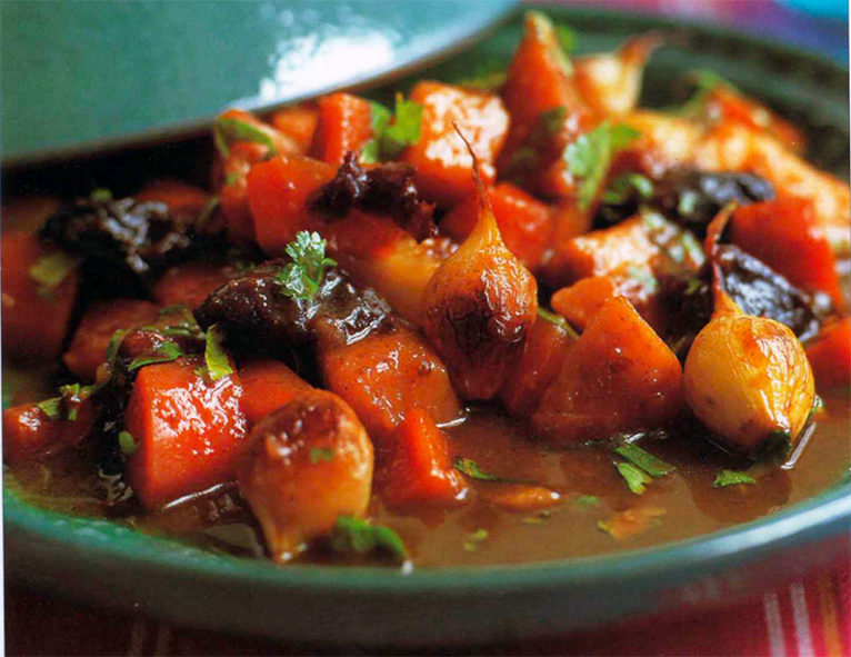 tagine of yam, carrots, prunes and baby onions shown served in a green tagine with the lid partially lifted