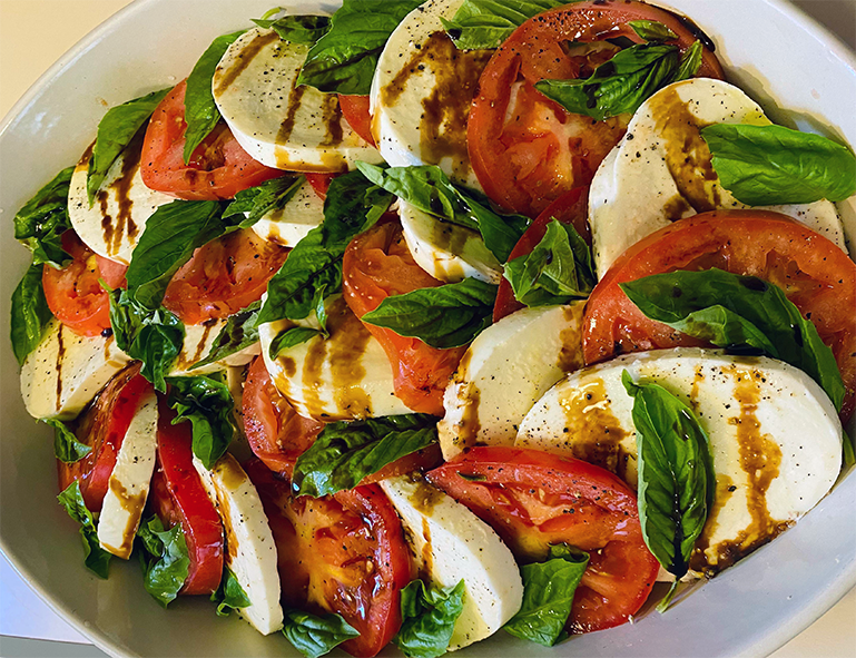 tomato and basil salad with sliced mozzarella cheese served drizzled with balsamic vinegar in a white dish
