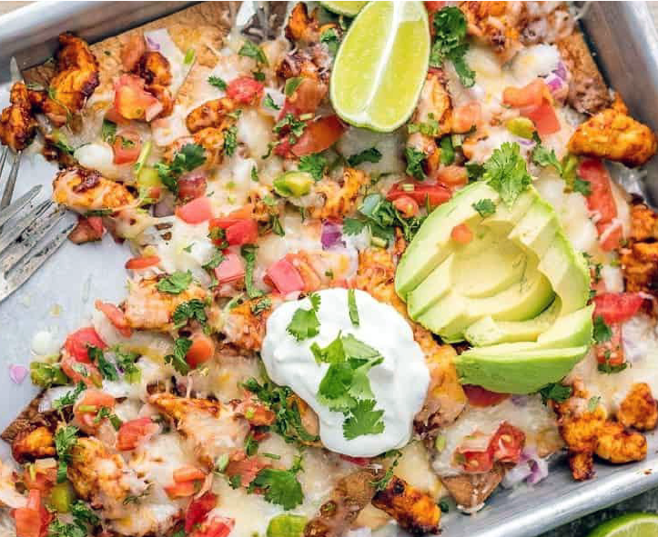 chicken baked with tortilla chips, queso dip, cheese and pico di gallo in a roasting tin serve topped with avocado