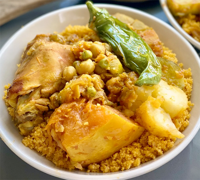 a bowl of couscous topped with chicken, pumpkin, fried sweet pepper and potatoes