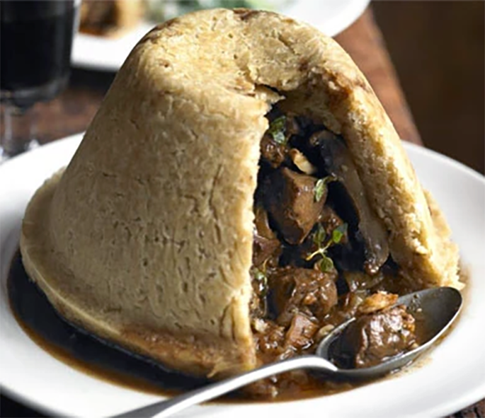steamed venison and mushroom suet pudding on a plate with a slice removed showing the filling