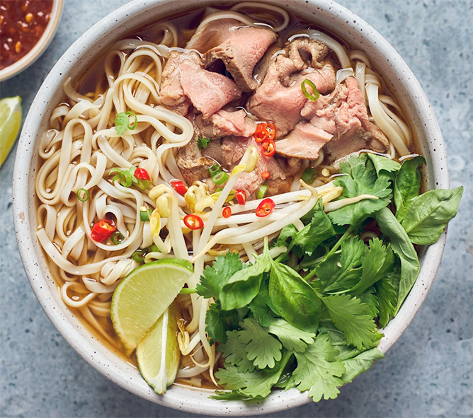 pho soup with beef, noodles noodles served in a bowl garnished with chillies, coriander leaves, beansprouts and lime wedges