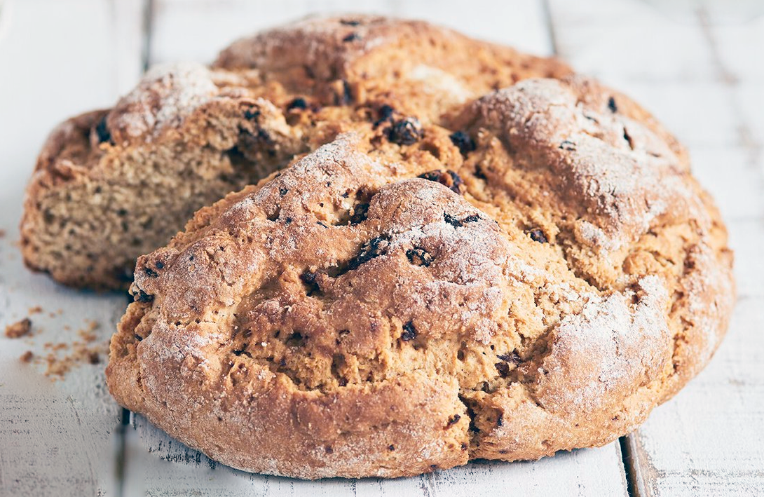 rustic wholemeal soda bread with a wedge removed on a white wooden table