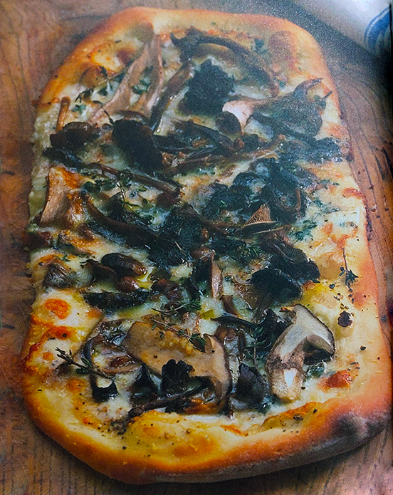 whole wild mushroom pizza shown on top of a wooden table
