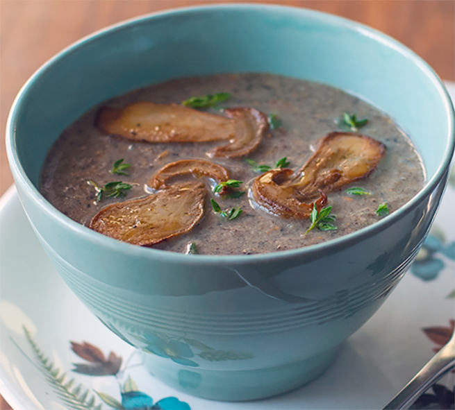 wild mushroom soup served in a blue bowl garnished with thyme leaves and fried bolete slices