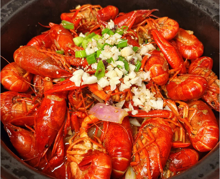 garlic braised crayfish in a cooking pot topped with chopped garlic and spring onions