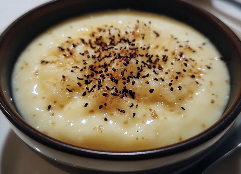 dessert of leftover rice in a custard base served in a bowl garnished with toasted and ground sesame seeds